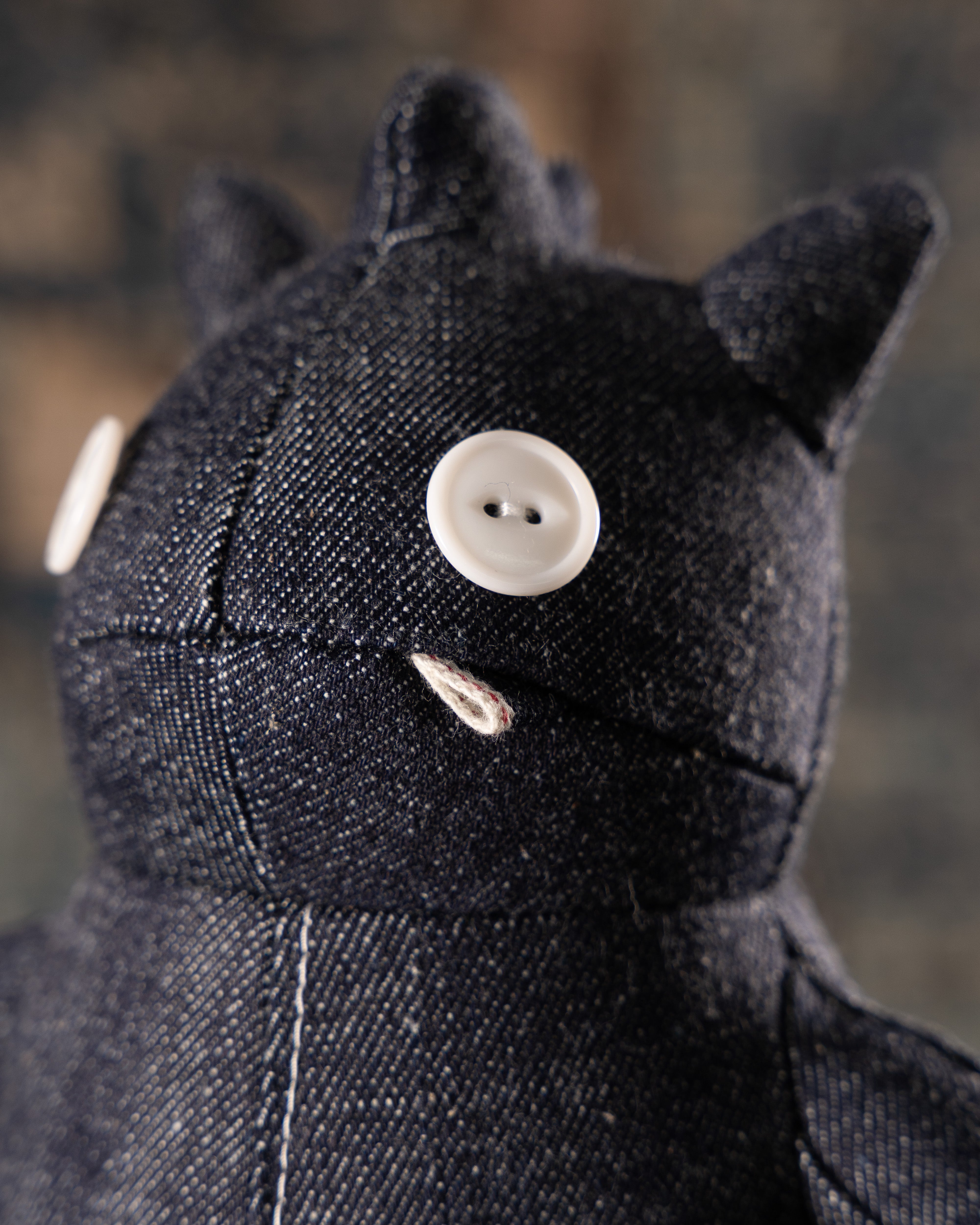 Black denim kaiju plush with a button for a face on a blurred background